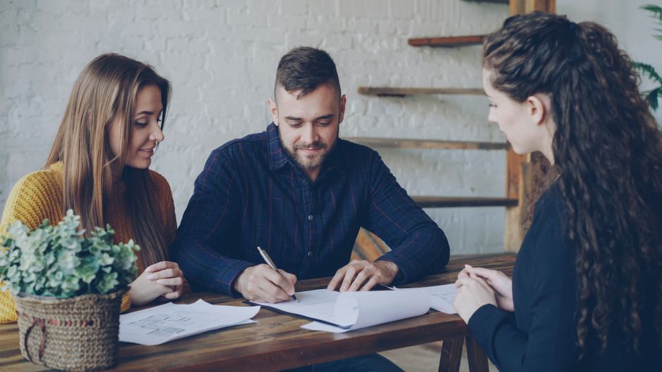 Couple signant un avant-contrat immobilier avec un notaire, des documents posés sur le bureau.